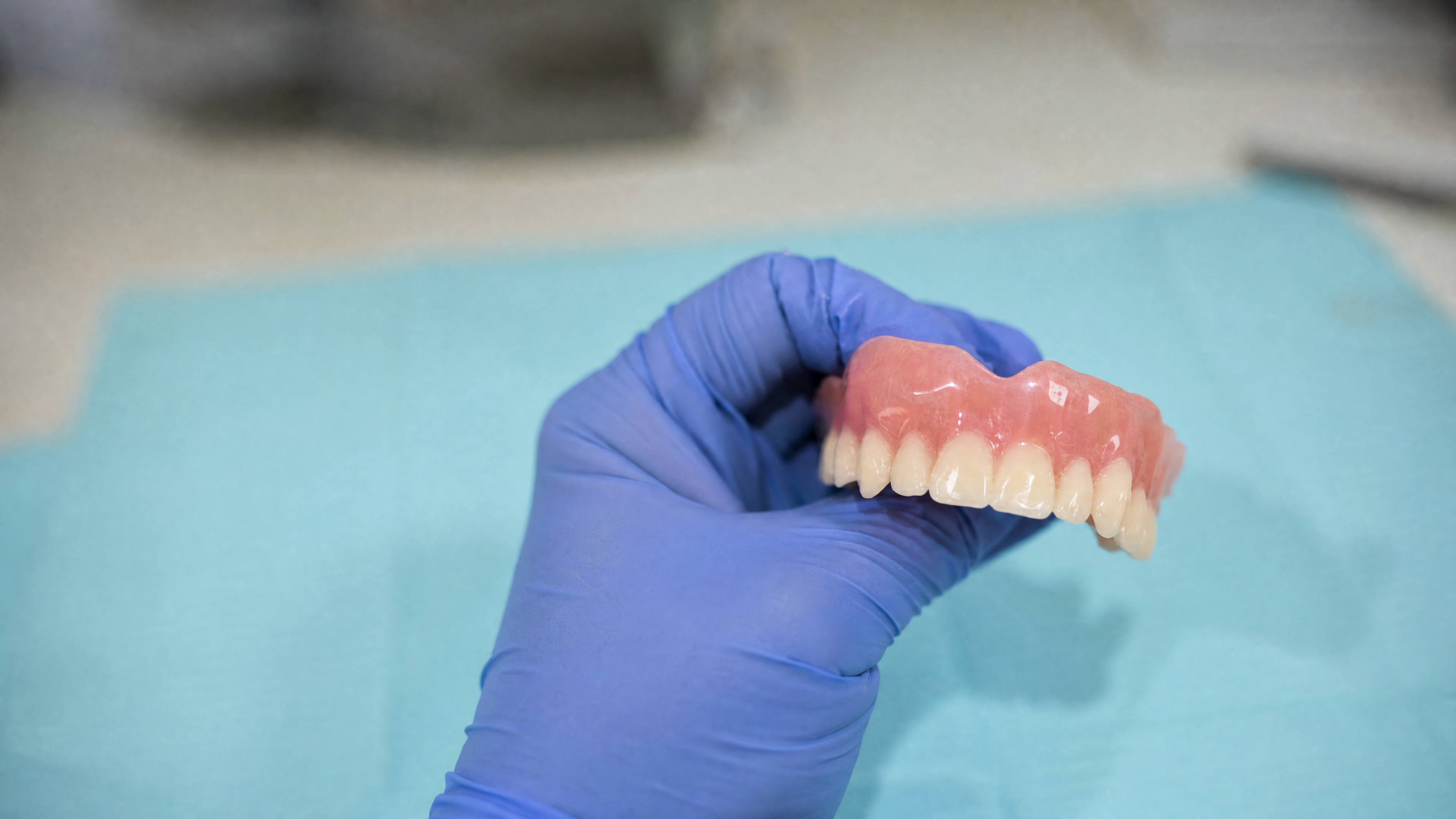 A gloved hand holding a finished upper denture in the laboratory
