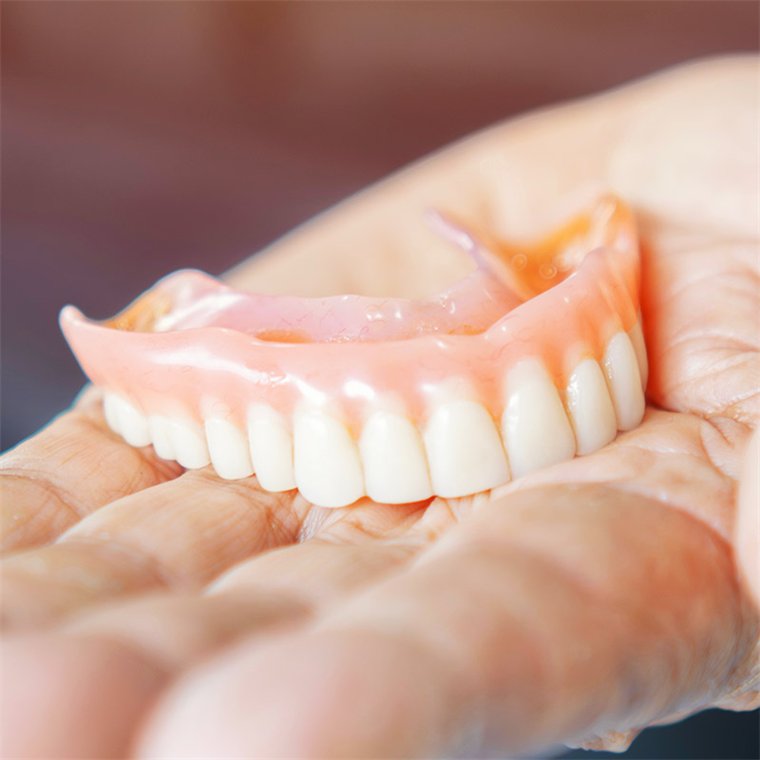 A newly finished denture resting on folded linen beside an instrument